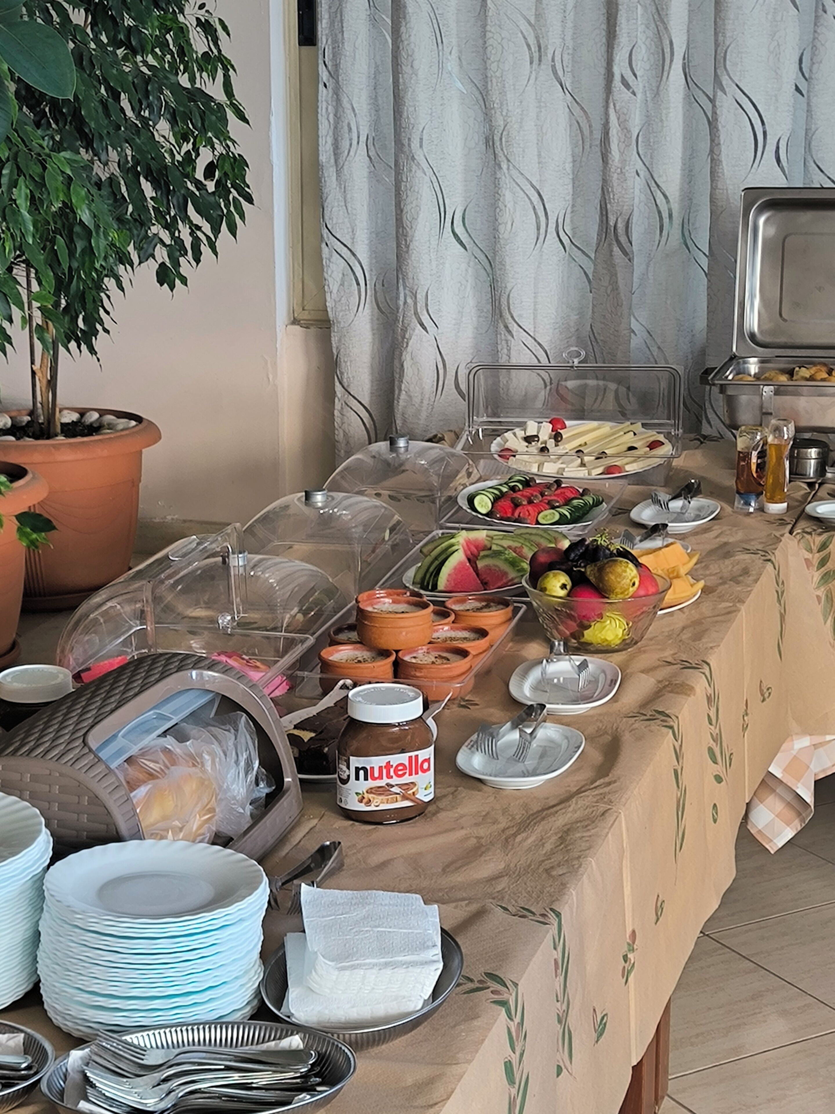 Una mesa de buffet con diferentes alimentos, entre ellos frutas, verduras y un tarro de Nutella.