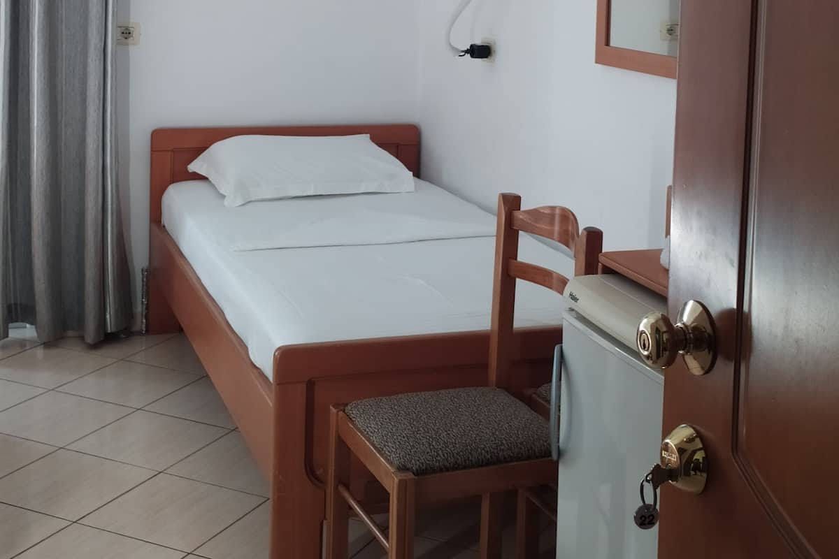 A hotel room with a bed, a chair, a desk, a television mounted on the wall, and an air conditioning unit.