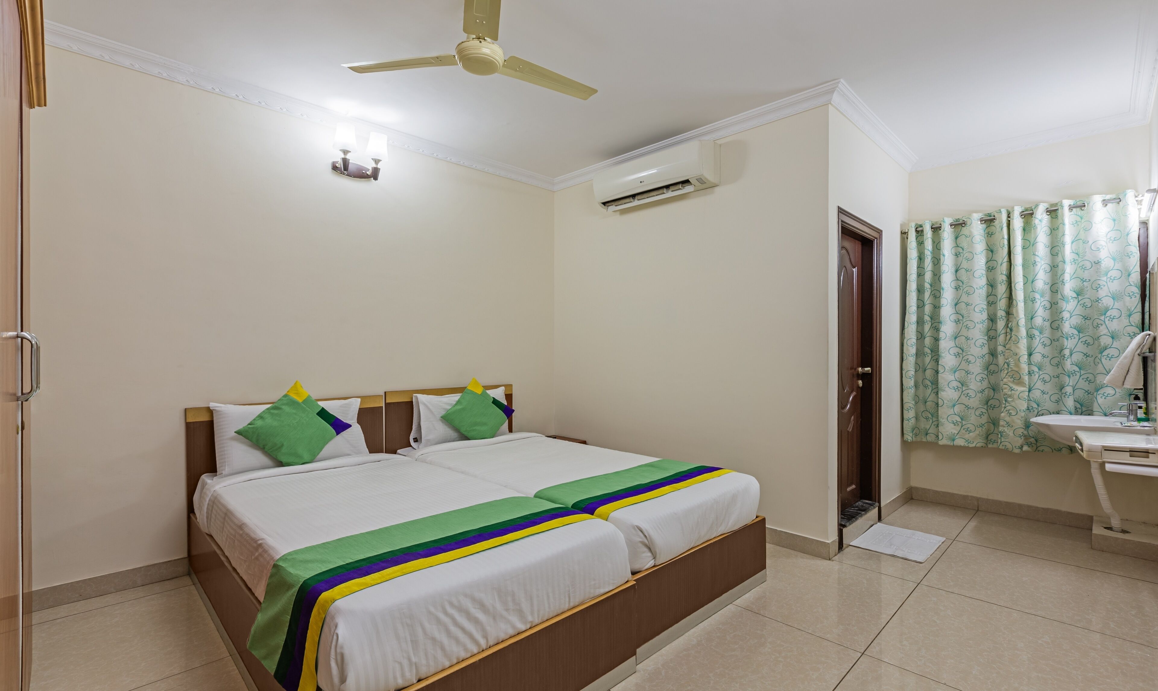 Habitación de hotel con cama, ventilador de techo, equipo de aire acondicionado, baño con lavamanos, inodoro y cortina de ducha.