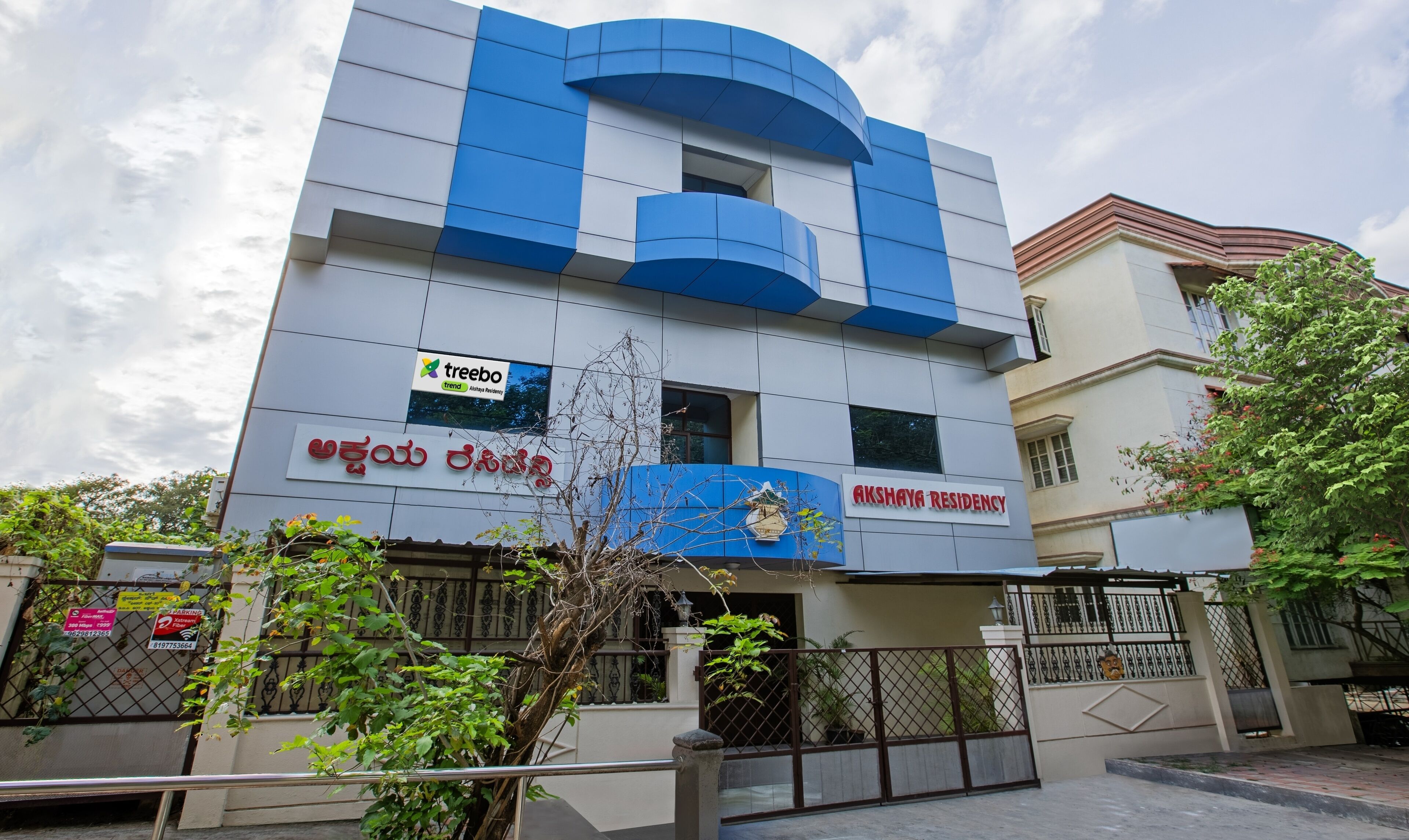 Un edificio moderno con un letrero que dice 'Akshaya Residency' y un letrero de 'Treebo' que indica un restaurante cercano.