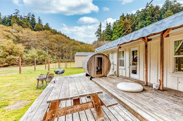 A wooden deck with a barrel, picnic table, and outdoor seating.
