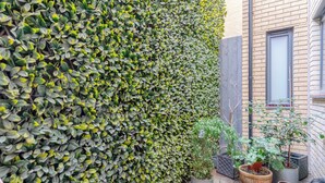 A garden area with a tall hedge, potted plants, and a brick building. - Modern 1 Bed | Private Patio | WiFi | East London (London)