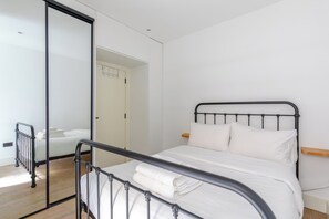A bedroom with a metal-framed bed, white bedding, a wooden nightstand, and a large mirror on the wall.
