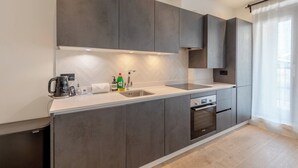 A modern kitchen with grey cabinets, a stainless steel sink, and a built-in oven. - Modern 1 Bed | Private Patio | WiFi | East London (London)