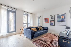 A modern living room with a blue sofa, a dining table, and a large window. - Modern 1 Bed | Private Patio | WiFi | East London (London)