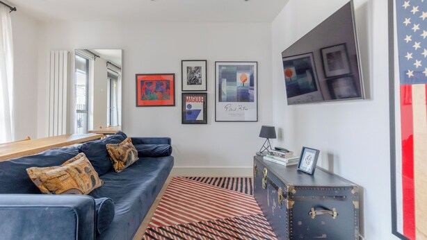 A modern living room with a dark blue sofa, patterned cushions, a striped rug, and a vintage suitcase on a side table. - Modern 1 Bed | Private Patio | WiFi | East London (London)