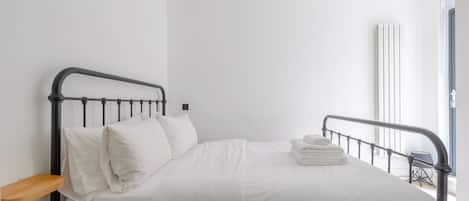A single bed with white bedding and pillows, a metal headboard, and a stack of folded towels on the footboard.