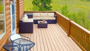 A wooden deck with outdoor furniture, including a sofa and a table, overlooking a grassy landscape. - Pet Friendly cabin w/ fireplace and mountain views (Jefferson)