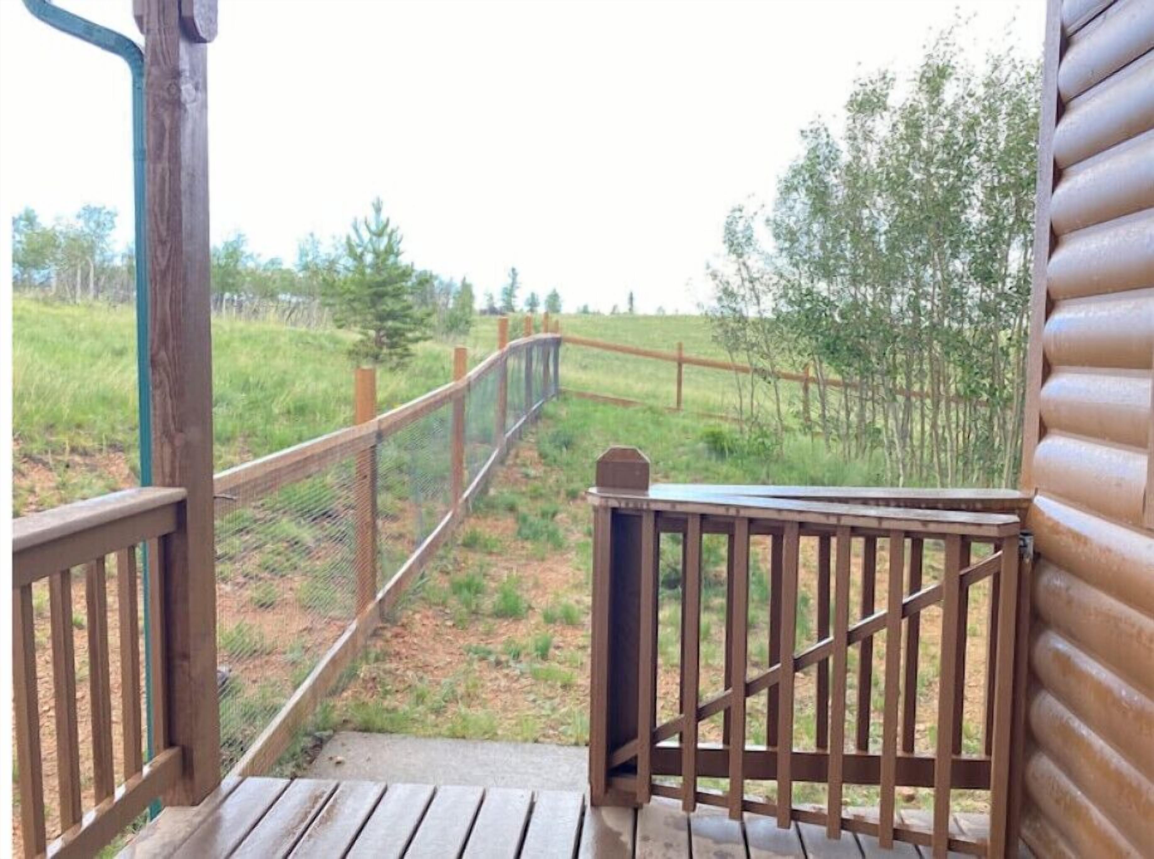 Een houten terras dat leidt naar een omheind gebied met uitzicht op bomen en gras.