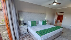 A spacious bedroom with a large bed, a bedside table with a lamp, a nightstand, and a ceiling fan. - Tembo Guest Lodge  (Mbombela)