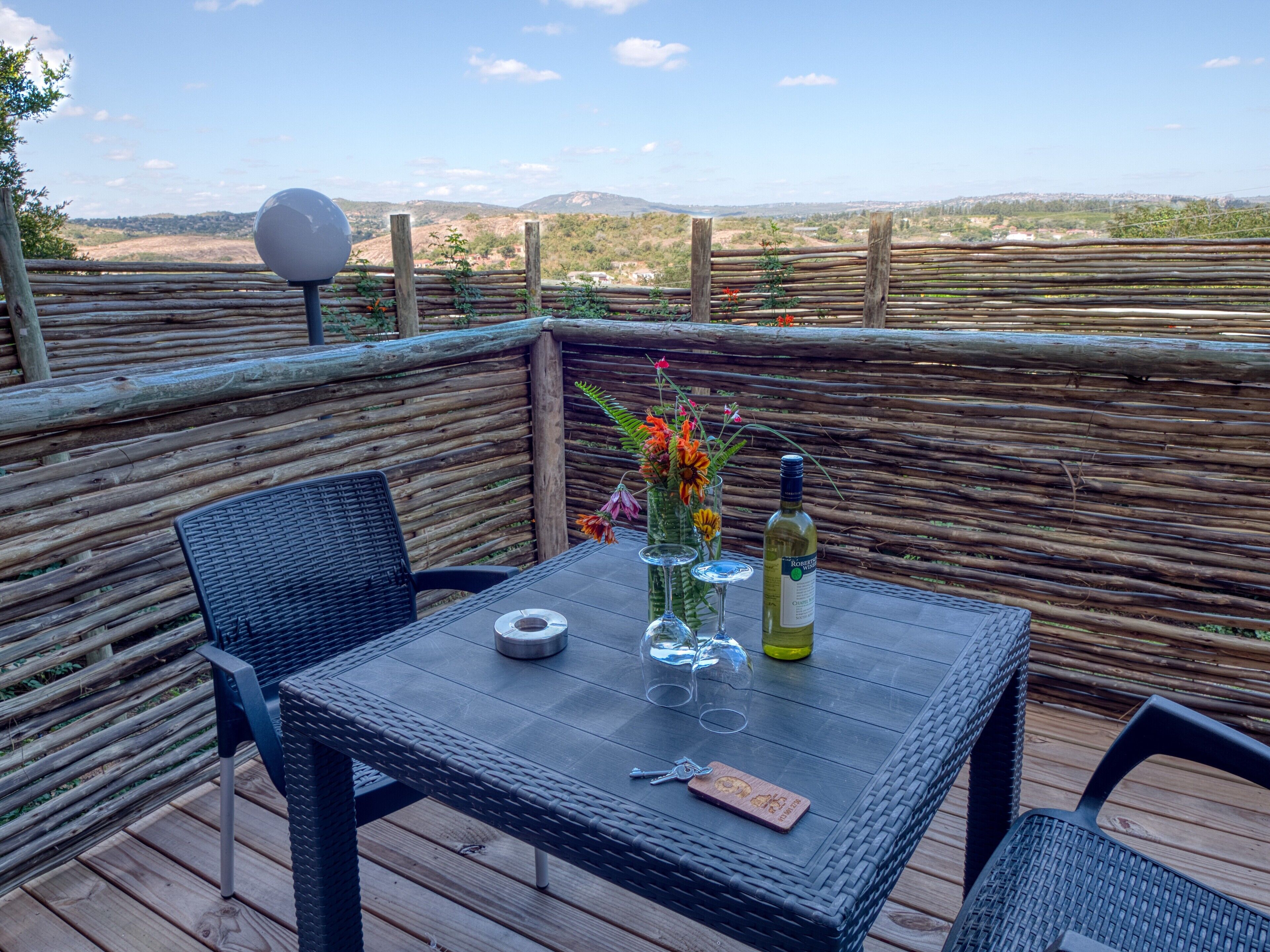 A table set outdoors with a bottle of wine, glasses, and a corkscrew on a wicker table.