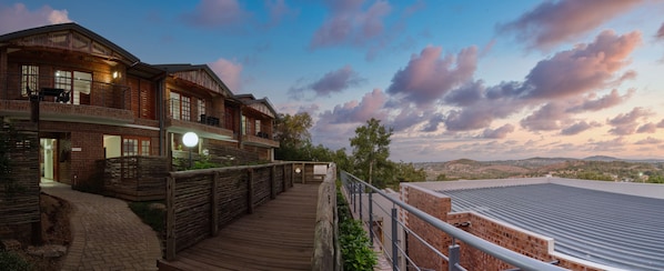 Un hotel con terraza de madera, fachada de ladrillo y vistas del paisaje circundante.
