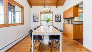 A modern kitchen with a wooden ceiling, a dining table with chairs, and a view of the outdoors. - Lakefront Midcentury Cottage (Williamson)