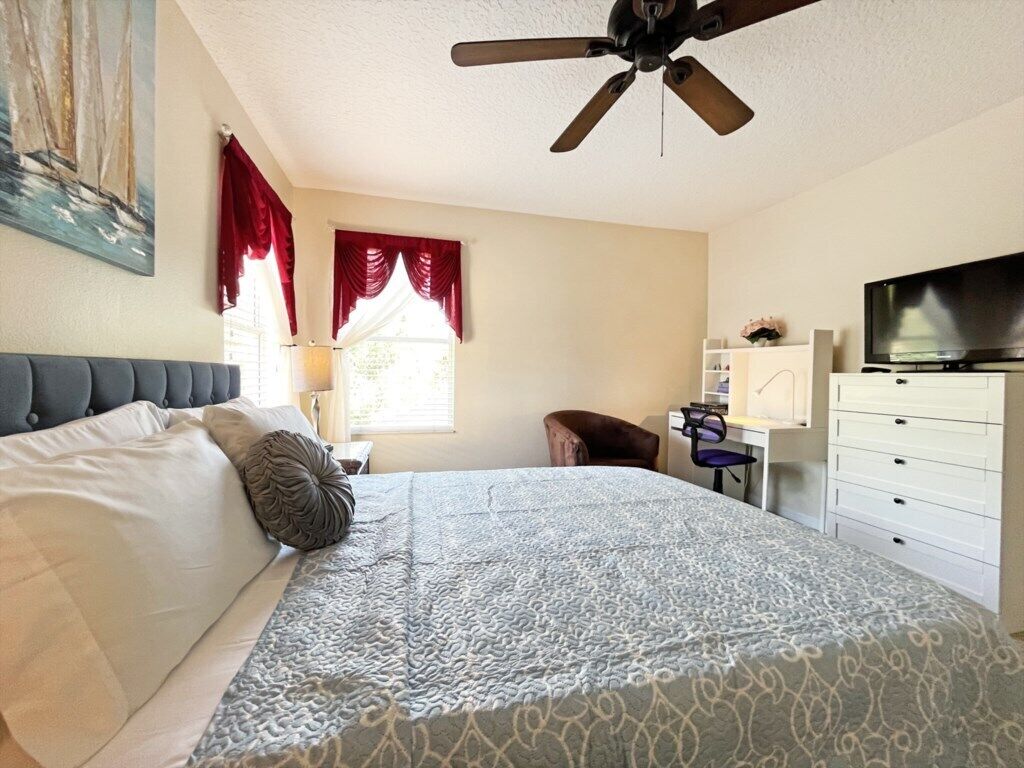 Ein Schlafzimmer mit Bett, Deckenventilator, Fernseher, Schreibtisch und Stuhl.