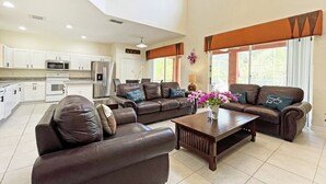 A spacious living area with a brown leather sofa, a wooden coffee table, and a kitchen in the background. - Bright resort villa with private pool overlooking conservation! (Kissimmee)