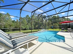 Une piscine extérieure couverte, dotée de chaises longues et d’un parasol rouge.