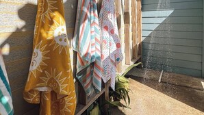 A wooden drying rack with colorful towels hanging on it, a water hose spraying water, and a house in the background. - MultiDeck VIEWS *Sleeps 14* Pool & PingPong Table *Games Galore* *Fire-Pit* (Galveston)
