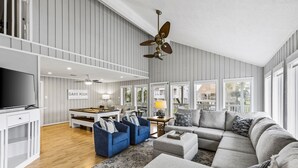 A spacious living room with a large sectional sofa, a flat-screen TV, and a ceiling fan. - MultiDeck VIEWS *Sleeps 14* Pool & PingPong Table *Games Galore* *Fire-Pit* (Galveston)