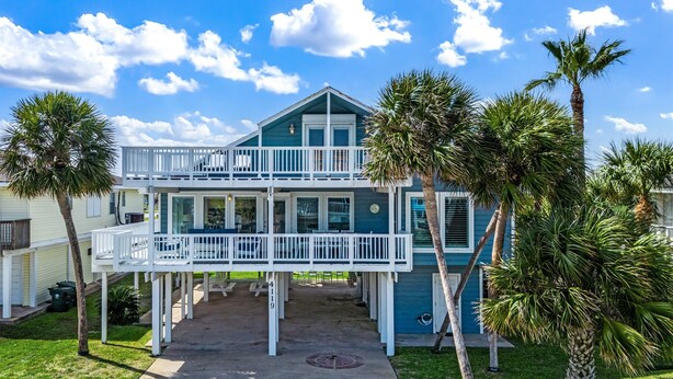 A two-story beachfront house with a balcony, palm trees, and a clear blue sky. - MultiDeck VIEWS *Sleeps 14* Pool & PingPong Table *Games Galore* *Fire-Pit* (Galveston)