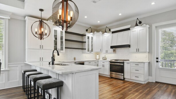 Una cocina moderna con armarios blancos, una isla central con taburetes de bar, un horno de acero inoxidable e iluminación colgante.
