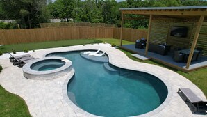 Un patio trasero con piscina, terraza de madera y zona de estar cubierta.