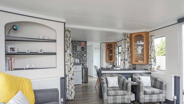 A cozy living room with a sofa, two armchairs, a dining table, and a kitchen area with a refrigerator and cabinets. - Rhiwlas Bach (Tyn-y-Gongl)