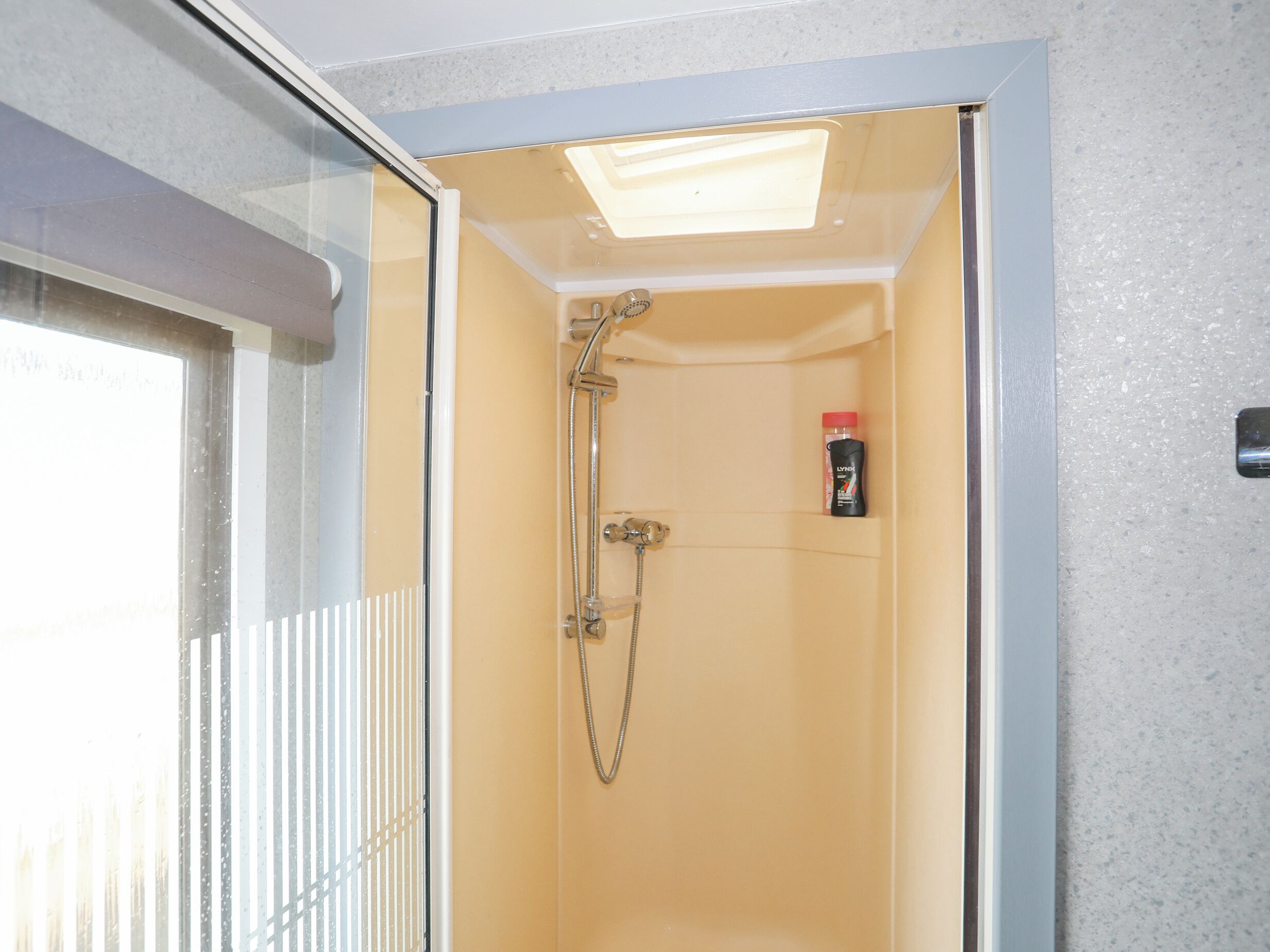 Un espacio de ducha pequeño y cerrado con puerta de vidrio, cabezal de ducha manual y una botella de champú en la pared.
