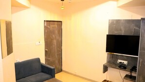 A room with a sofa, a small table, a television mounted on a wall, and a door.