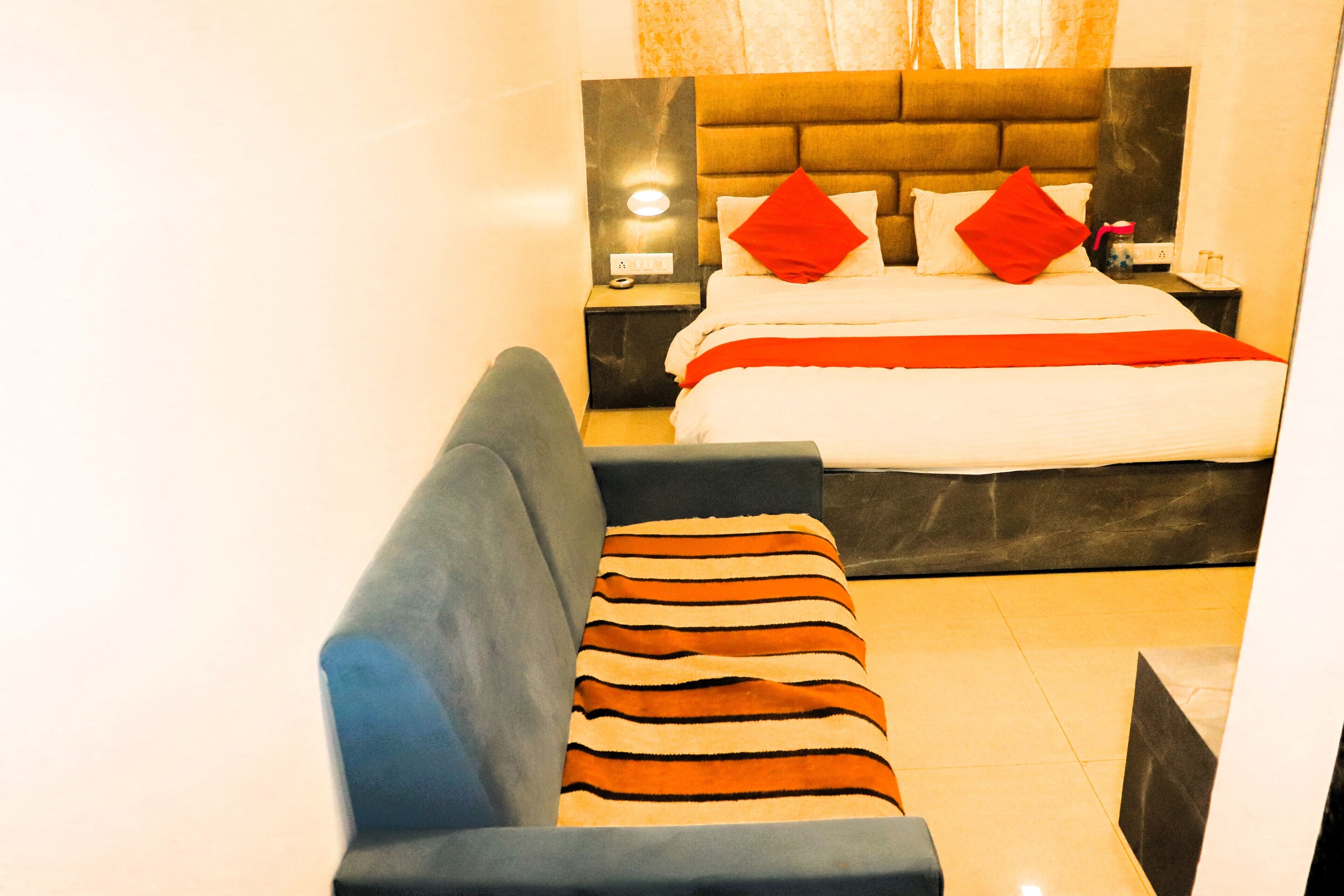 A modern hotel room with a bed, a nightstand, a lamp, and a sofa.