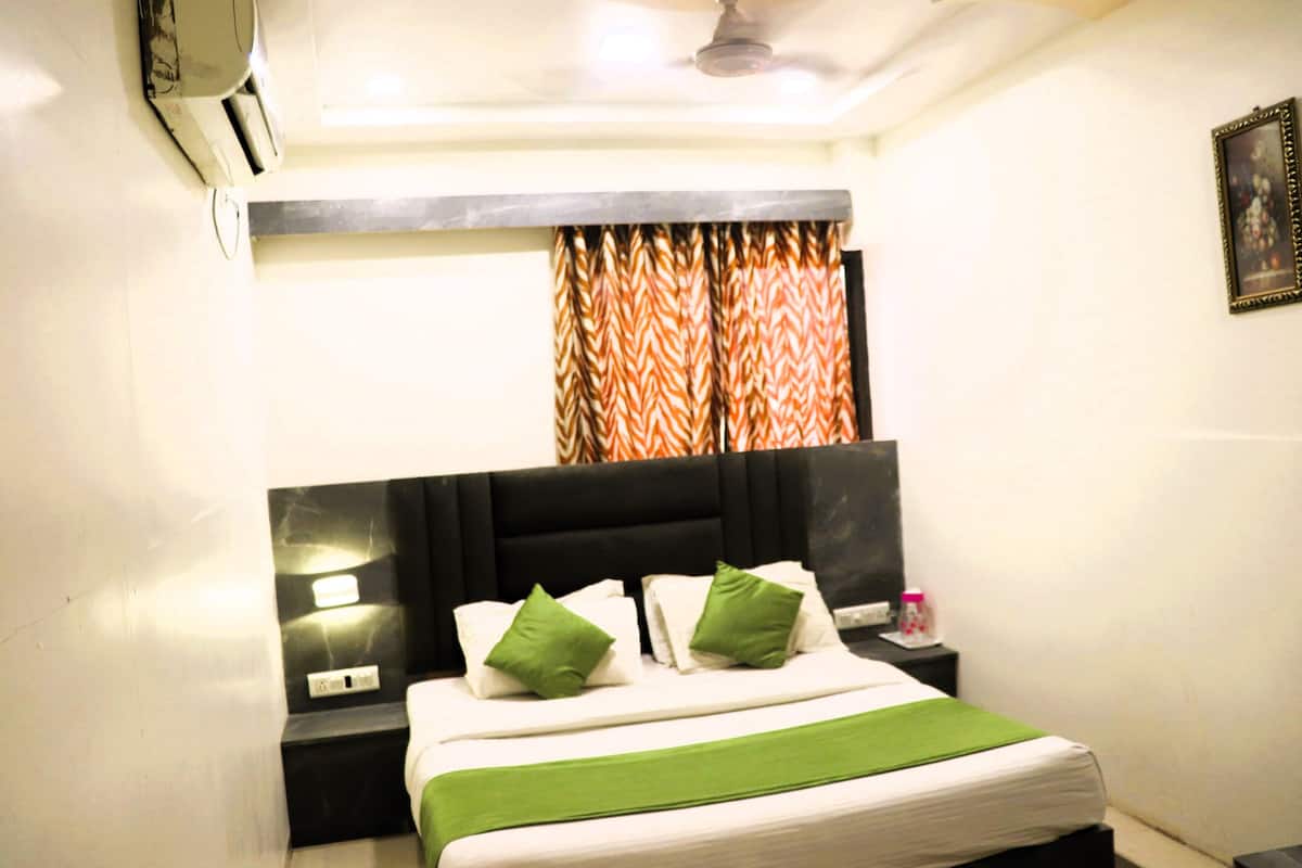 A neatly made bed with green pillows, a black headboard, and a window with patterned curtains.