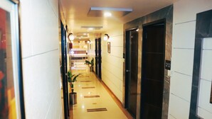 A hotel hallway with a tiled floor, potted plants, and doors leading to rooms.