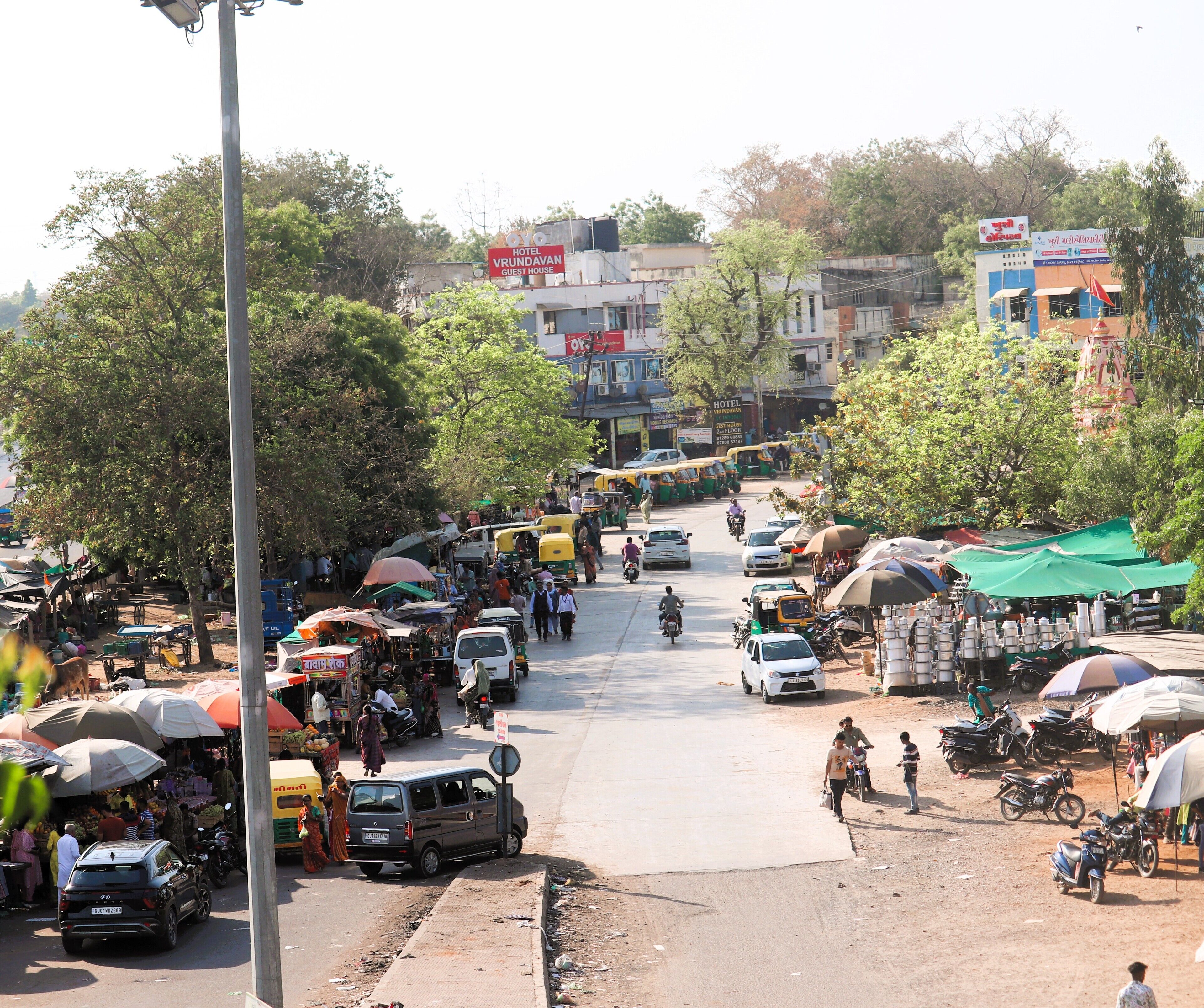 A busy street with a hotel named 'Hotel Vrundavan Guest House' in the background.