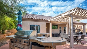 An outdoor patio with a stone grill, seating area, and a pergola. - AMAZING Pool home with outdoor kitchen, firepit, and waterfall Close 2 Casinos!  (Bullhead City)