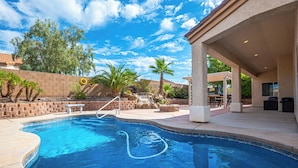 A swimming pool with a stone border, palm trees, and a covered patio area. - AMAZING Pool home with outdoor kitchen, firepit, and waterfall Close 2 Casinos!  (Bullhead City)