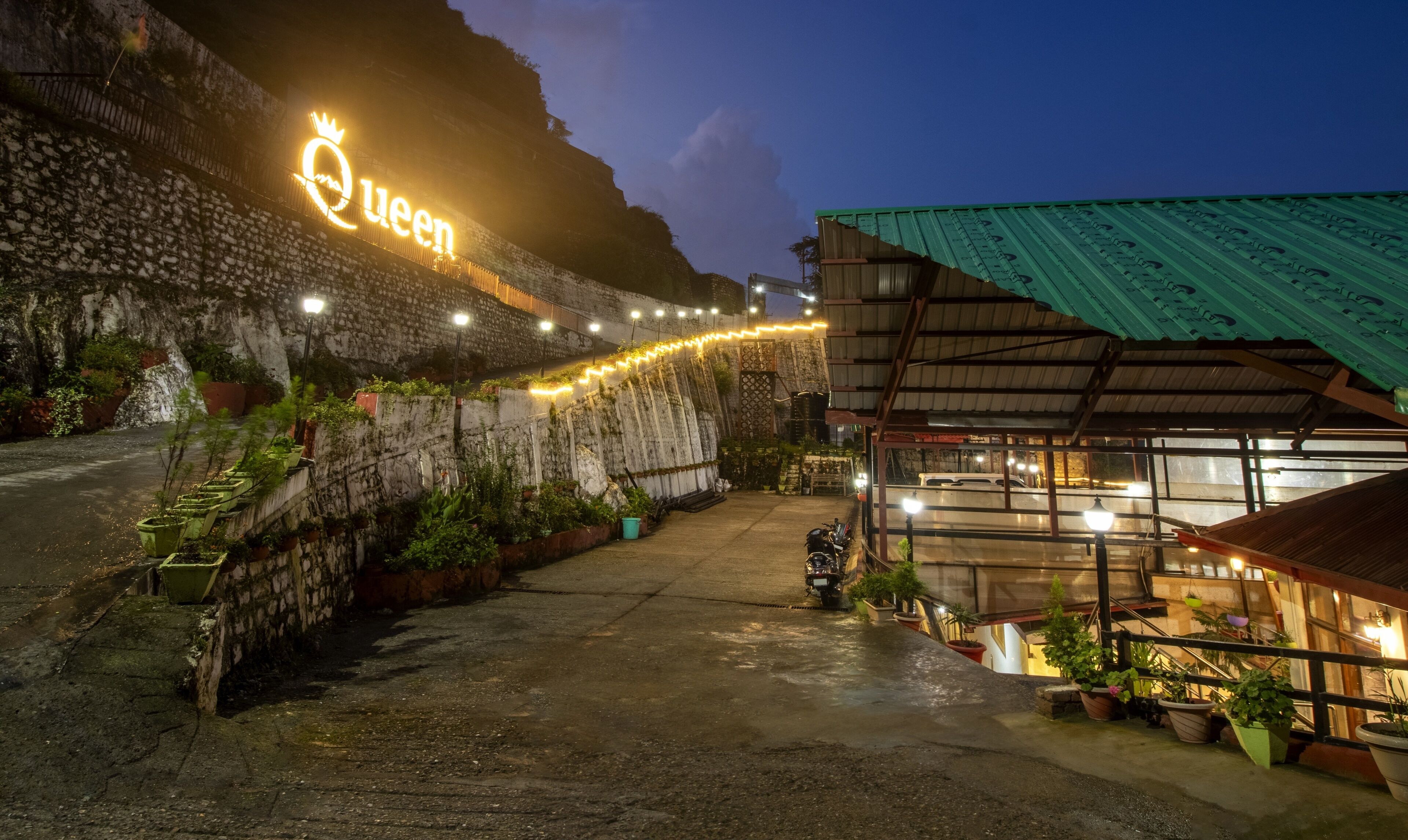 Un hotel con un letrero de neón que dice "Queen" y una pared de piedra con plantas.