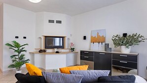 Un salon moderne avec un canapé, un téléviseur, une plante et un tableau accroché au mur.