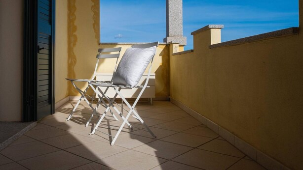 Un balcon avec une chaise pliante et une petite table, un sol carrelé et un mur jaune.