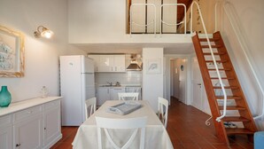A kitchen with white cabinets, a dining table with chairs, a refrigerator, and a staircase leading to an upper level. - Casa Petralana by Wonderful Italy (Olbia)