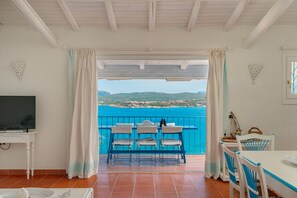 Un balcón con mesa y sillas, un televisor y vista al mar.