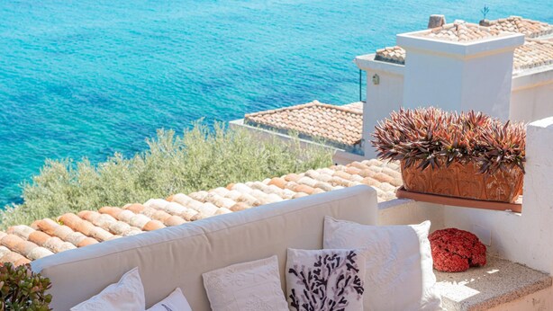 A white outdoor seating area with cushions, a potted plant, and a view of the sea. - Casa Azzurra by Wonderful Italy (Olbia)