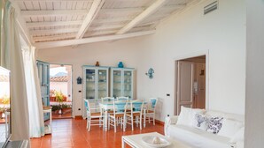 A spacious living area with a white sofa, a dining table with blue chairs, and a kitchen visible through an open door. - Casa Azzurra by Wonderful Italy (Olbia)