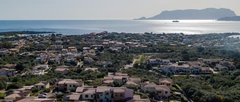 A coastal town with a mix of traditional and modern buildings, a clear view of the sea, and a distant mountain.
