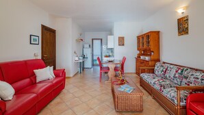 A living room with a red sofa, a patterned sofa, a coffee table, and a dining area with chairs and a table. - Casa Helen by Wonderful Italy (Olbia)