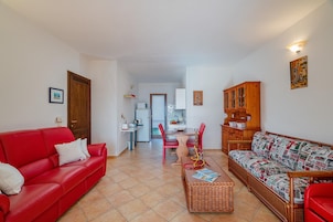 Una sala de estar con un sofá rojo, un sofá estampado, una mesa de centro y un comedor con sillas y una mesa.