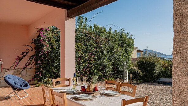 An outdoor dining area with a table set for four, surrounded by wooden chairs, a blue folding chair, and a tablecloth. - Casa Helen by Wonderful Italy (Olbia)