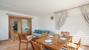 A dining area with a wooden table set for four, surrounded by wooden chairs. There is a sofa with blue cushions in the background, and a sliding glass door leading to an outdoor area. - Sweet Mavy Incantevole Dimora by Wonderful Italy (Olbia)