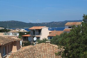 A coastal residential area with terracotta-tiled roofs, a satellite dish, and a view of the sea and boats in the background. - Casa Julia by Wonderful Italy (Olbia)