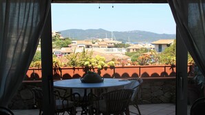 A patio with a round table and chairs, overlooking a hillside with buildings and a wind turbine.