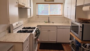 A compact kitchen with white cabinets, a gas stove, a dishwasher, and a microwave.