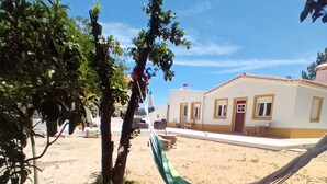 A sandy outdoor area with a hammock, a tree, and a building with a red door. - O Mundo da Lua Casa Este (São Simão)